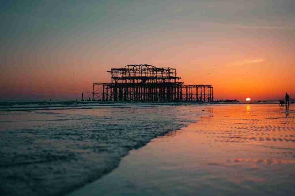 orange sunset sky with the old Brighton pier silhouette and the sea on the beach