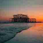 orange sunset sky with the old Brighton pier silhouette and the sea on the beach