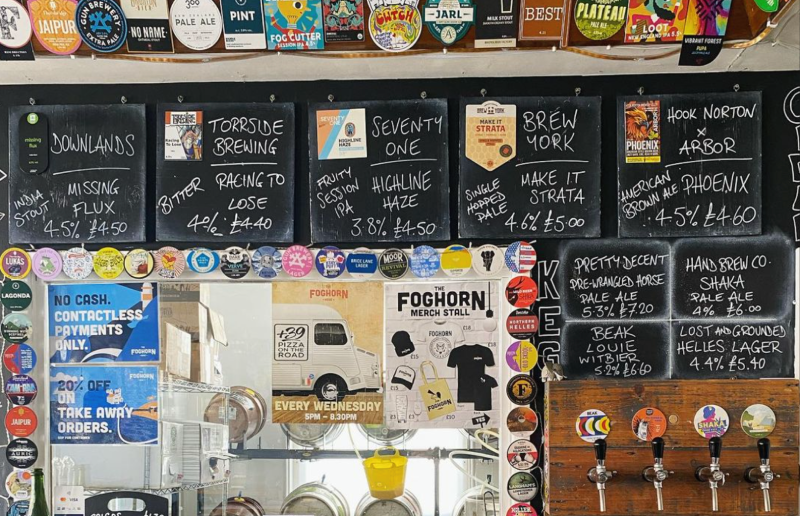 Interior shot of The Foghorn pub, with a busy bar where there are many handwritten chalk signs for different beers, local to Brighton and Sussex
