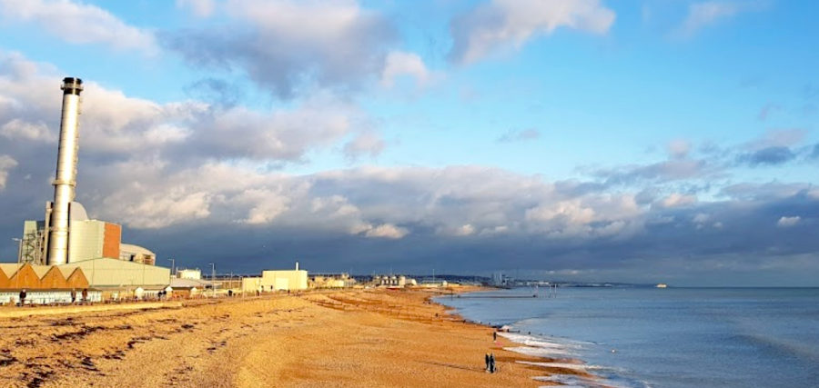 A wide angle shot of Southwick beach. There is a tall metal factory chimney on the left and a blue sky with dramatic clouds