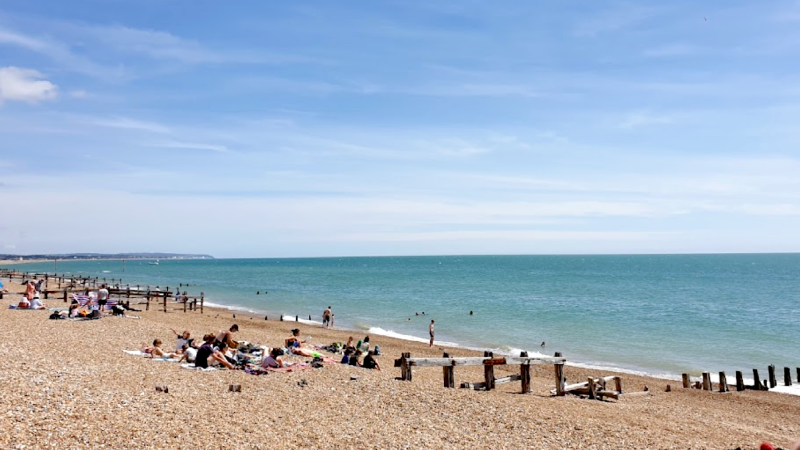 A wide shot of a typical British beach. Blue sky and blue sea with some people enjoying the weather sat down.