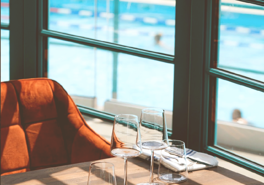 A stylish shot of wine glasses, a designer burnt orange dining chair and a swimming pool in the background that can be seen through the window.