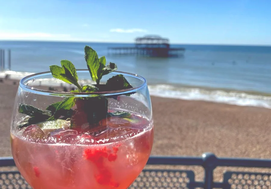 red cocktail with garnish, with Brighton beach and the old pier in the background