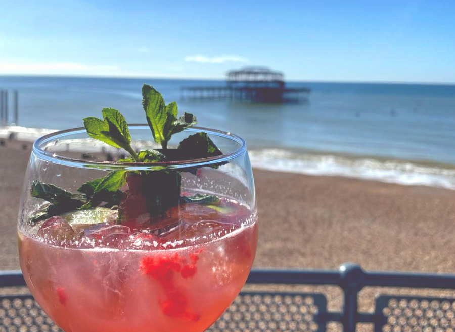 red cocktail with garnish, with Brighton beach and the old pier in the background