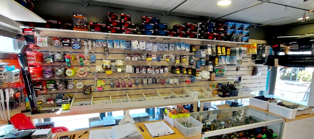 The inside of a fishing tackle shop. There are lots of items on the wall and stacked on a shelf above the till.