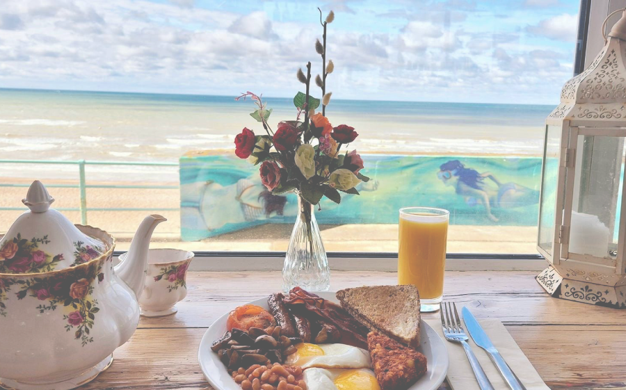 A classic British beach cafe with a classic English breakfast, floral tea pot, orange juice and view of the sea.