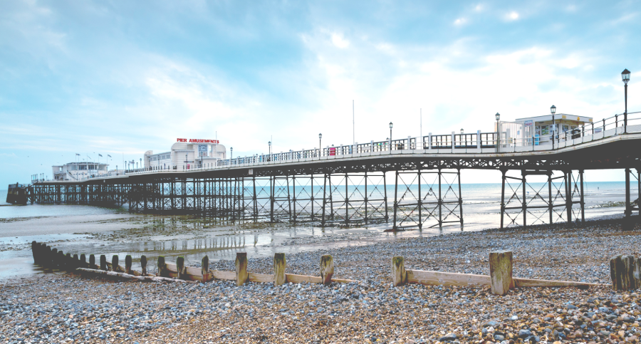 A wide angle shot from the pebble beach of a classic British seaside pier with a blue sky in the background